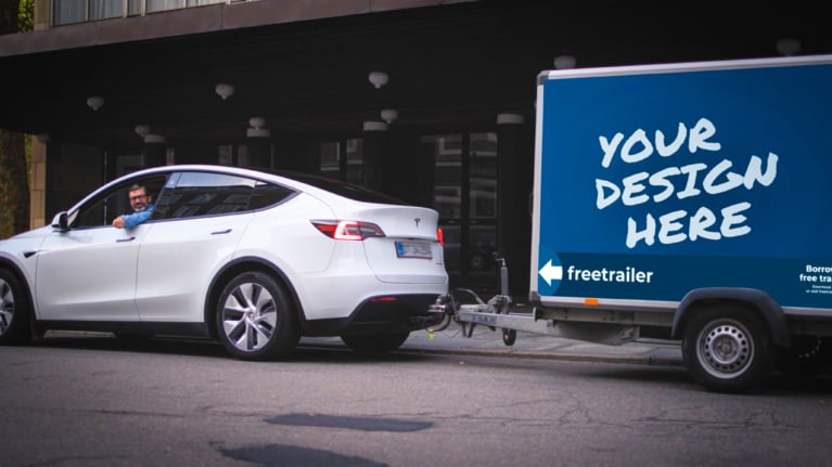 White Tesla towing a Freetrailer advertising trailer with “Your Design Here” graphic, showcasing branding opportunities for businesses looking to become partner.