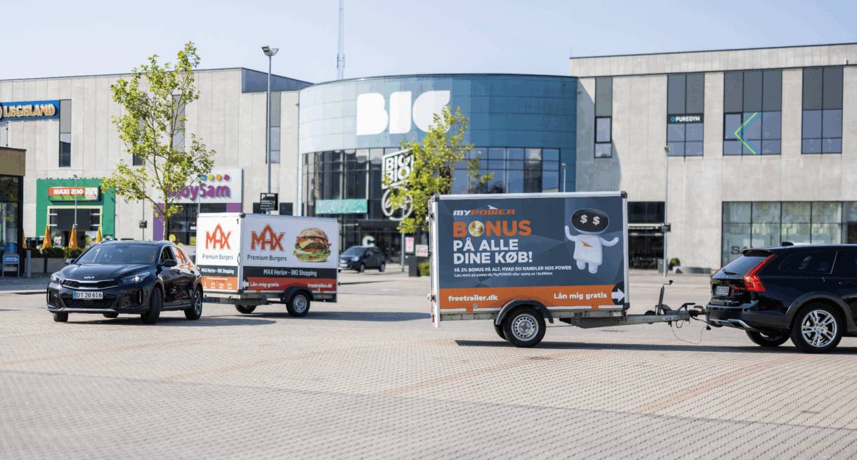 Two cars pulling branded Freetrailer trailers in front of the BIG Shopping center in Herlev, Denmark—one promoting MAX Burgers and the other POWER. A visual example of how businesses can increase exposure and foot traffic through branded trailers.