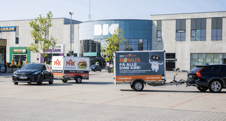 Two cars pulling branded Freetrailer trailers in front of the BIG Shopping center in Herlev, Denmark—one promoting MAX Burgers and the other POWER. A visual example of how businesses can increase exposure and foot traffic through branded trailers.